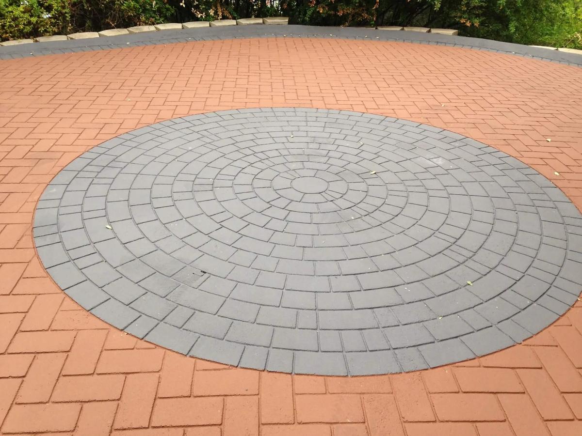 Decorative asphalt courtyard featuring a circular herringbone stamped pattern bordered in red brick tone