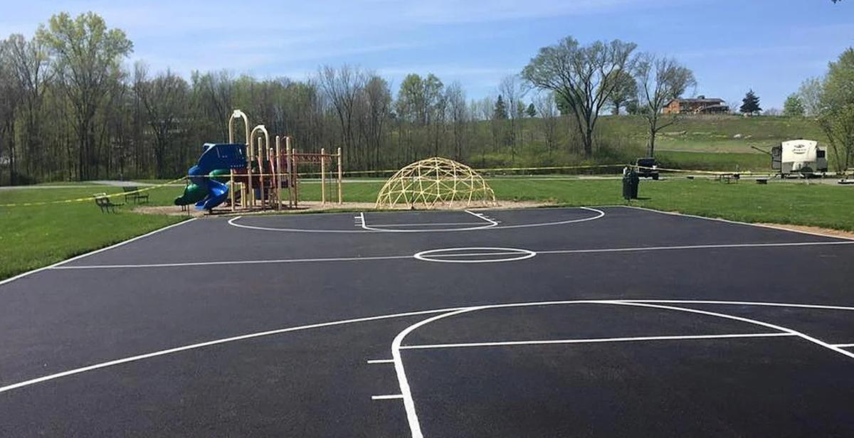 Playground paving completed — a freshly paved basketball court and walkway area next to playground equipment