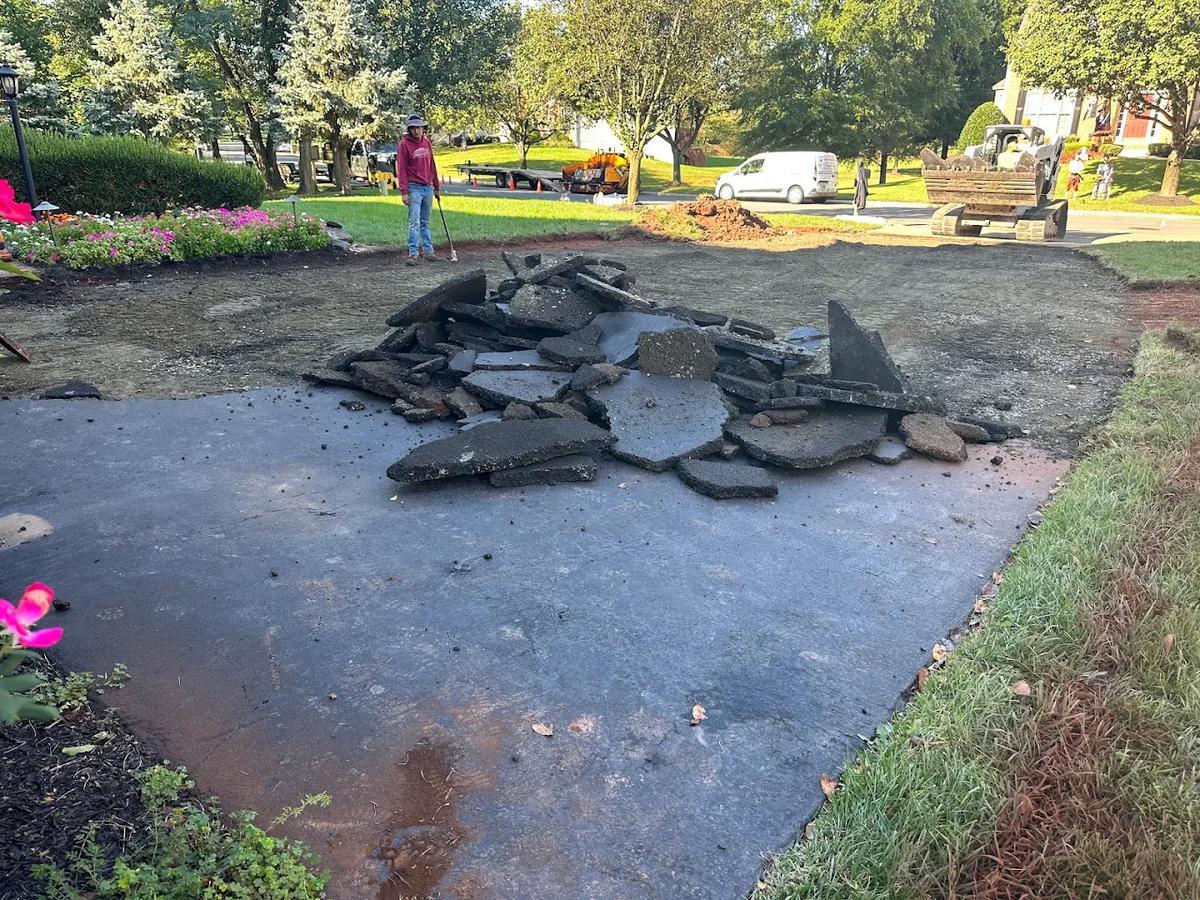 Removing a blacktop driveway down to the base in Northern Virginia — broken asphalt pieces cleared and piled before new paving begins