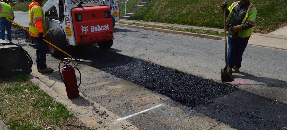Utility trench paving in progress — a crew restoring asphalt over a utility trench cut across a residential street